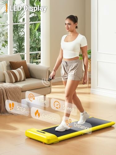 Woman walking on a yellow treadmill in a living room with LED display showing step count, time, speed, calories, and distance.